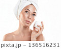 Beautiful Caucasian woman with white towel wrapped around her head. She holds cream jar in hand, isolated on white. 136516231