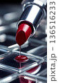 Macro shot of a vibrant red lipstick with liquid pigment dripping onto a reflective glass tile grid. 136516233