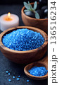 Blue sea salt in wooden bowls for spa treatment with a lit candle and massage stones on a dark background. 136516234