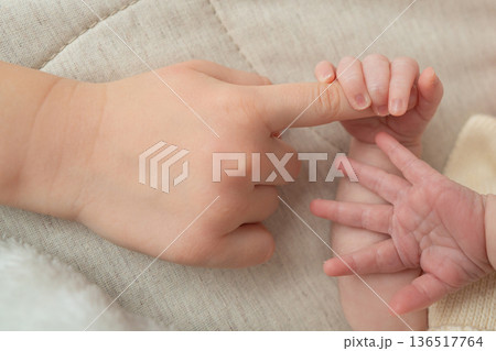Close-up shot of a newborn baby hand gently holding the finger of an older child. The image focuses on connection, care, and family bond, symbolizing protection, love, and tenderness between siblings Close-up shot of a newborn baby hand gently holding the finger of an older child. The image focuses on connection, care, and family bond, symbolizing protection, love, and tenderness between siblings 136517764