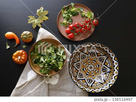 Multicolored ceramic plates and patterned bowl with vegetables and herbs on black background. Food and traditional cuisine. Top view. 136518497
