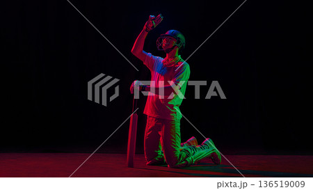 Cricket player celebrating on knees raising hand under neon lights. 136519009