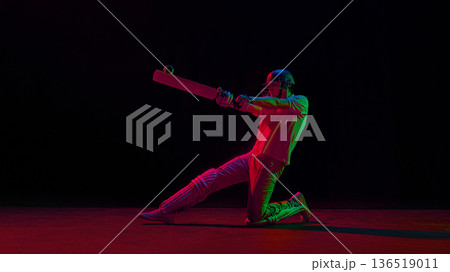 Cricket player sliding on knee while striking ball under neon lighting. Cricket player sliding on knee while striking ball under neon lighting. 136519011