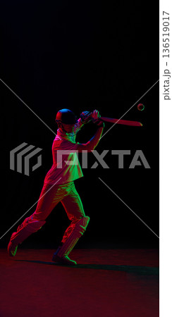 Cricket player hitting ball under red and green neon lighting 136519017