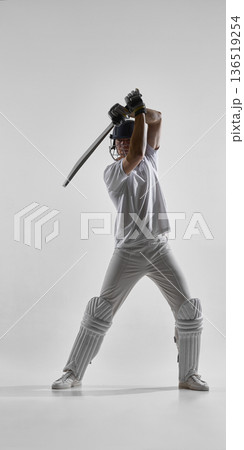 Cricket player holding bat ready to strike isolated on white background 136519254