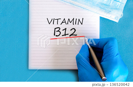 Vitamin B12 symbol. Concept words Vitamin B12 on beautiful white note. Doctor's hand in blue medical glove. Medical mask. Beautiful blue background. Medical healthy lifestyle Vitamin B12 concept. Vitamin B12 symbol. Concept words Vitamin B12 on beautiful white note. Doctor's hand in blue medical glove. Medical mask. Beautiful blue background. Medical healthy lifestyle Vitamin B12 concept. 136520042
