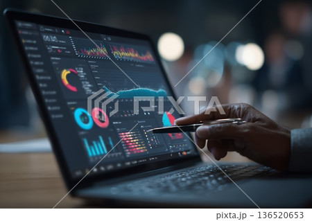 Close-up of a hand pointing at analytical graphs and detailed data on a laptop screen during a business meeting. 136520653