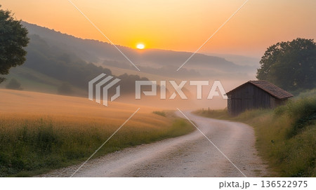 Tranquil sunrise over misty countryside path with rustic barn 136522975