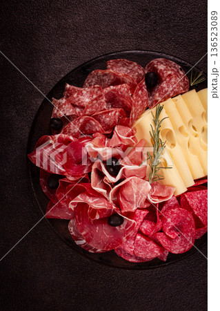 Cold cuts, appetizer, prosciutto, salami and ham, with maasdam cheese and olives, on a round plate, breakfast, top view, close-up, deserted 136523089