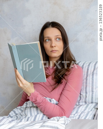 young woman is reading book in bed. In morning, female makes entries in diary, mental health. 136523189