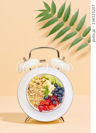 Alarm clock with a bowl instead of a clock face. The bowl is filled with different breakfast foods, including strawberries, blueberries, kiwi Alarm clock with a bowl instead of a clock face. The bowl is filled with different breakfast foods, including strawberries, blueberries, kiwi 136523207