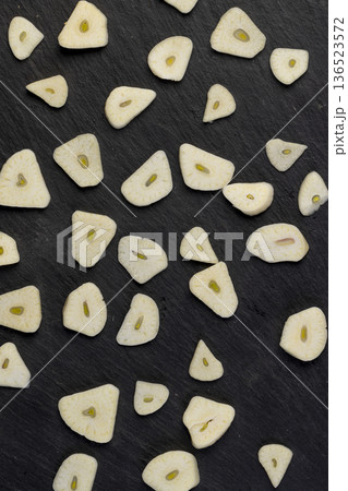 peeled and sliced garlic cloves scattered on black slate , peeled and sliced natural and fresh spices from garlic cloves scattered on black slate stone 136523572