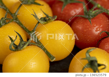 wet round fresh and sweet tomatoes of red and yellow color lie on the table, yellow tomatoes with dots on the peel, a large number of freshly picked tomatoes covered with drops of water 136523579