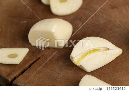 peeled and sliced purple garlic scattered on the black kitchen table and peeled and sliced fresh and natural garlic spices scattered on the kitchen table during cooking 136523612