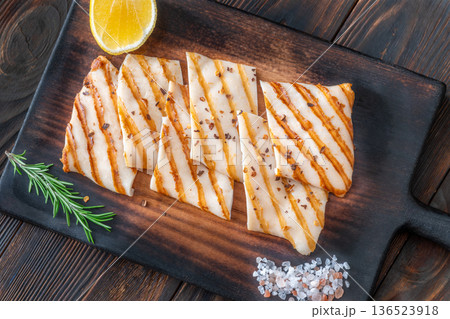 Grilled squid steaks with rosemary and lemon on dark wooden cutting board Grilled squid steaks with rosemary and lemon on dark wooden cutting board 136523918