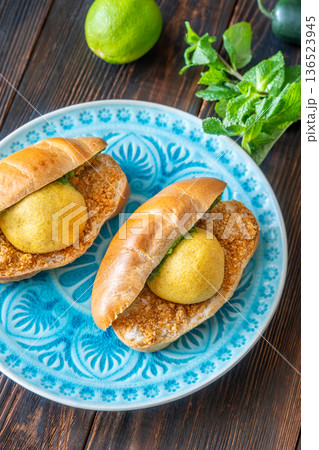 Authentic Vada Pav Indian street food with spicy chutney on rustic wooden background Authentic Vada Pav Indian street food with spicy chutney on rustic wooden background 136523945