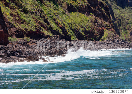 Waves crash on volcanic stones near Porto Moniz, Madeira, where green cliffs meet clear blue seas 136523974