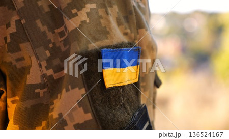 Close up of military blue-yellow chevron on shoulder of soldier at countryside. This emblem embodies the unbreakable spirit and pride of the ukrainian people. Concept of invasion resistance 136524167