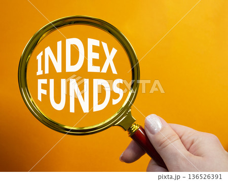 Index Funds symbol. Magnifying Glass with words Index Funds. Businessman hand. Beautiful orange background. Business and Index Funds concept. Copy space. 136526391