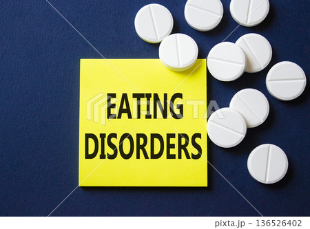 Eating Disorders symbol. Concept word Eating Disorders on yellow note. Beautiful deep blue background with pills. Medicine and Eating Disorders concept. Copy space Eating Disorders symbol. Concept word Eating Disorders on yellow note. Beautiful deep blue background with pills. Medicine and Eating Disorders concept. Copy space 136526402