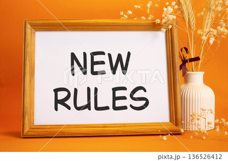 New rules symbol. Concept words New rules on beautiful wooden picture frame. Beautiful orange background with flower vase. Business and New rules concept. Copy space. New rules symbol. Concept words New rules on beautiful wooden picture frame. Beautiful orange background with flower vase. Business and New rules concept. Copy space. 136526412