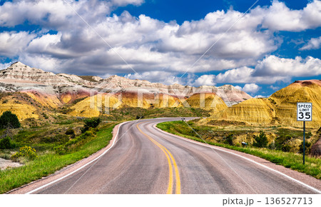 Badlands Loop Road in Badlands National Park South Dakota. Scenic winding road features a speed limit sign and colorful Yellow Mounds geologic formations under a cloudy sky 136527713