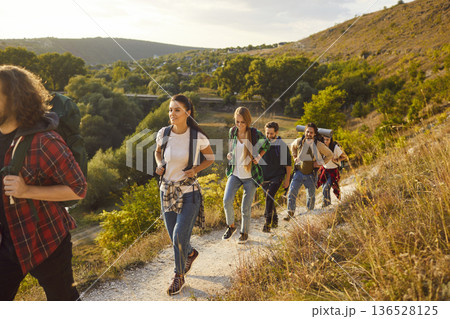 Group of people with backpacks hiking or trekking on mountain trail among beautiful nature 136528125