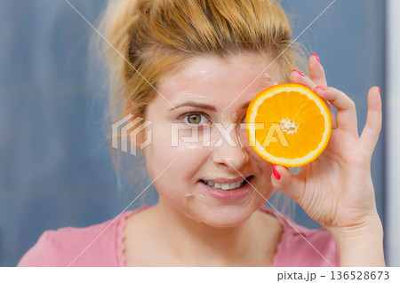 Woman having gel mask on face holding orange 136528673