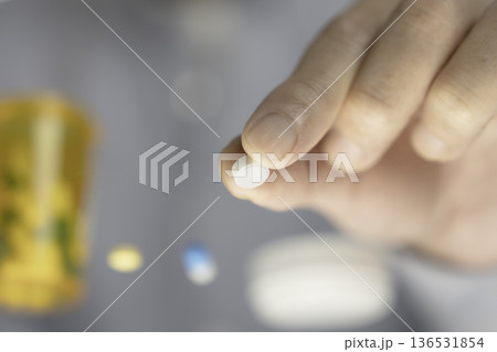 服用前の白い錠剤を指でつまむクローズアップ 136531854