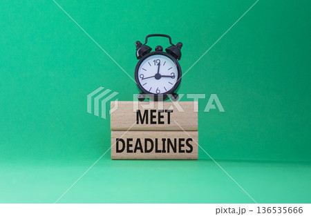 Meet Deadlines symbol. Concept word Meet Deadlines on wooden blocks. Beautiful green background with alarm clock. Business and Meet Deadlines concept. Copy space Meet Deadlines symbol. Concept word Meet Deadlines on wooden blocks. Beautiful green background with alarm clock. Business and Meet Deadlines concept. Copy space 136535666