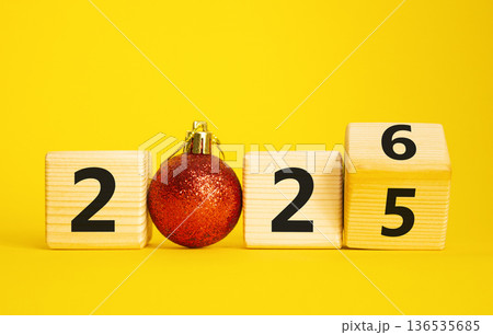 2026 New Year symbol. Businessman turns wooden cube and changes Year 2025 to 2026. Beautiful yellow background with Christmas ball. Copy space. Business and 2026 happy new year concept 136535685