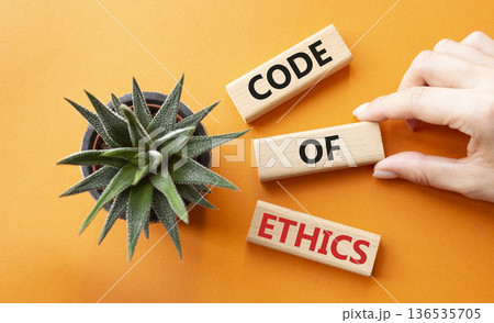 Code of ethics symbol. Concept words Code of ethics on wooden blocks. Businessman hand. Beautiful orange background with succulent plant. Business and Code of ethics concept. Copy space. Code of ethics symbol. Concept words Code of ethics on wooden blocks. Businessman hand. Beautiful orange background with succulent plant. Business and Code of ethics concept. Copy space. 136535705