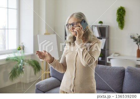 Old senior woman talking on phone at home, gesturing for family, friend, doctor communication  136539200