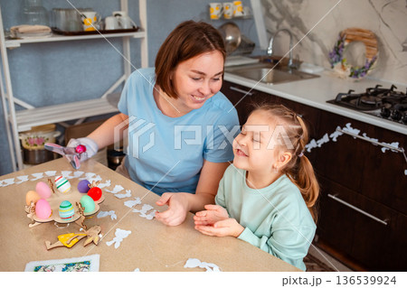 Mid shot of mother and happy little daughter play together, sitting at the Easter table. Top view. Happy family leisure 136539924