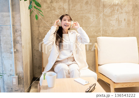 カフェのソファーに座りヘッドホンで音楽を聴く女性 136543222
