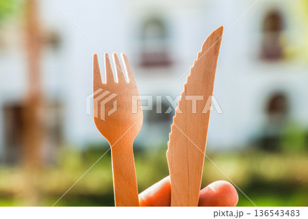 A pair of wooden cutlery fork and knife in hand on bokeh nature background A pair of wooden cutlery fork and knife in hand on bokeh nature background 136543483