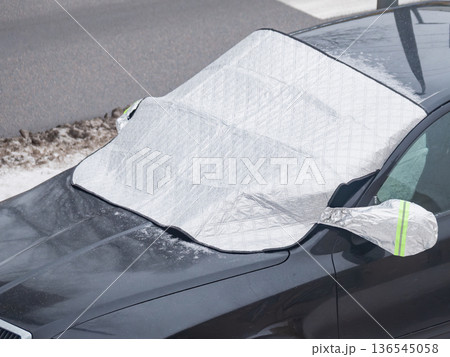 A car is parked on a snowy street with a tarpaulin covering its windshield. A car is parked on a snowy street with a tarpaulin covering its windshield. 136545058