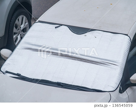 A car is parked on a snowy street with a tarpaulin covering its windshield. A car is parked on a snowy street with a tarpaulin covering its windshield. 136545059