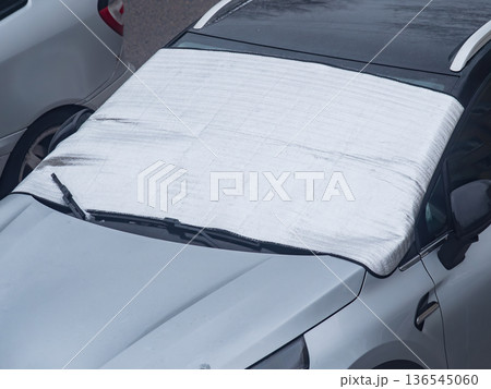A car is parked on a snowy street with a tarpaulin covering its windshield. A car is parked on a snowy street with a tarpaulin covering its windshield. 136545060