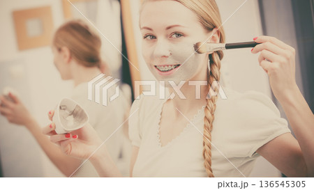 Happy young woman applying mud mask on face Happy young woman applying mud mask on face 136545305
