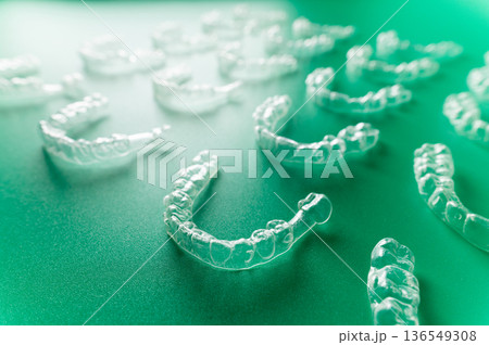 Clear dental aligners arranged on a green surface, showcasing multiple orthodontic trays designed for teeth straightening and alignment treatment Clear dental aligners arranged on a green surface, showcasing multiple orthodontic trays designed for teeth straightening and alignment treatment 136549308