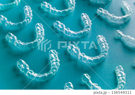 Clear orthodontic aligners arranged on a blue surface, showcasing their transparent design and dental structure for teeth straightening treatment Clear orthodontic aligners arranged on a blue surface, showcasing their transparent design and dental structure for teeth straightening treatment 136549311