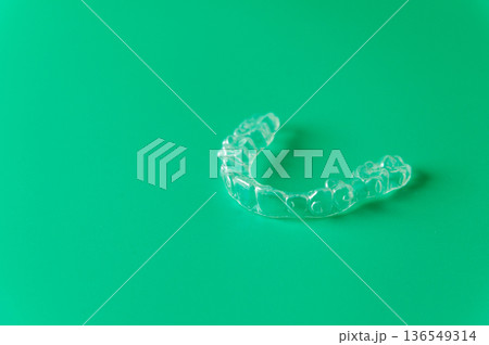Clear dental aligner placed on a vibrant green background, showcasing its transparent design and unique shape for orthodontic treatment and teeth straightening 136549314