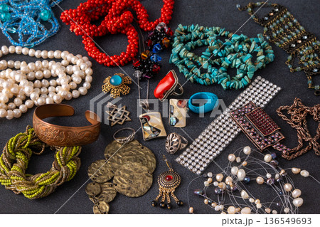 Collection of vintage and bohemian jewelry, featuring turquoise beads, pearl necklaces, coral pieces, silver rings, and brass bracelets scattered on a dark textured background Collection of vintage and bohemian jewelry, featuring turquoise beads, pearl necklaces, coral pieces, silver rings, and brass bracelets scattered on a dark textured background 136549693