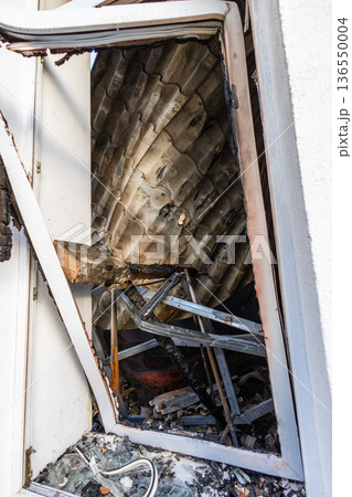 Bila Tserkva, Kyiv region, Ukraine 09.06.2025: Charred interior seen through a broken window, with scorched roof tiles, burnt beams, and scattered debris after a severe fire. Bila Tserkva, Kyiv region, Ukraine 09.06.2025: Charred interior seen through a broken window, with scorched roof tiles, burnt beams, and scattered debris after a severe fire. 136550004