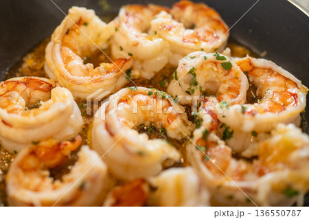 Shrimp scampi cooking in a pan with sizzling garlic, butter, and herbs, preparing a delicious seafood meal Shrimp scampi cooking in a pan with sizzling garlic, butter, and herbs, preparing a delicious seafood meal 136550787