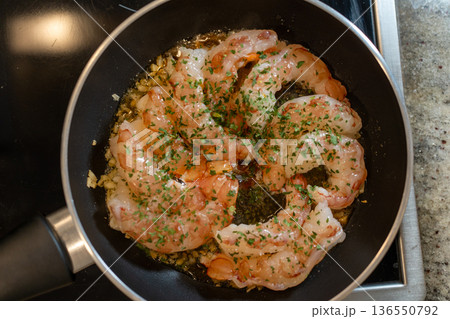 Shrimp sautéing in olive oil with garlic and parsley in a frying pan on the stove — fresh, homemade seafood meal preparation 136550792