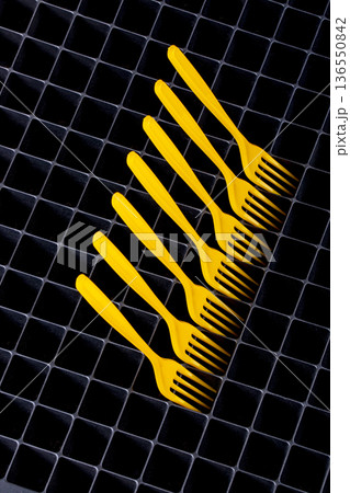 Still life with yellow plastic forks on a surface with cells. Still life with yellow plastic forks on a surface with cells. 136550842