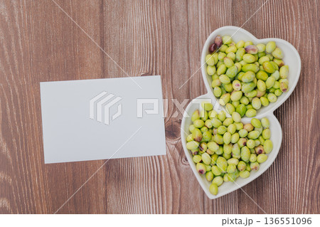 Freshly harvested green olives in heart shaped plate on wooden table, Mediterranean superfood rich in vitamins with blank paper for copy space 136551096