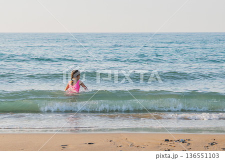 Little girl swimming in sea with blank copy space, child playing in ocean waves during summer vacation, family travel and water resort concept 136551103